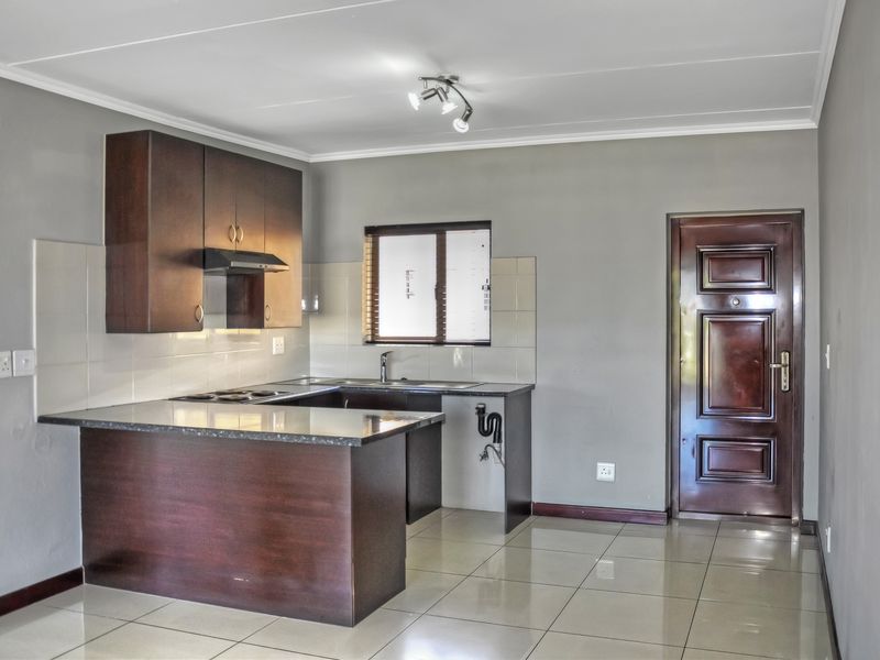 A functional kitchen featuring dark wood cabinetry, granite countertops, built-in hob, and tiled flooring, with an adjacent solid wood entrance door.