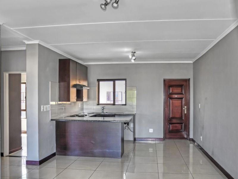 Open plan living area featuring a compact kitchen with dark cabinetry, granite countertops, and tiled flooring, leading to a solid wood entrance door.