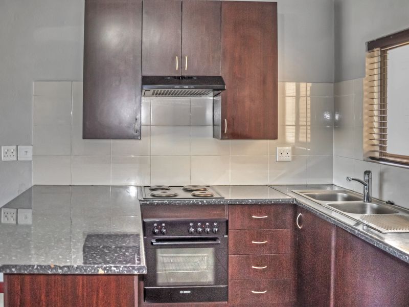 A functional kitchen featuring dark wood cabinetry, laminate countertops, a built-in oven with electric hob, and a double bowl stainless steel sink.