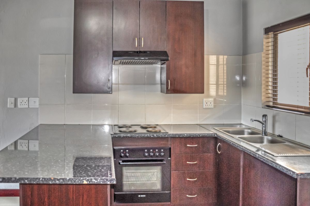 A functional kitchen featuring dark wood cabinetry, laminate countertops, a built-in oven with electric hob, and a double bowl stainless steel sink.