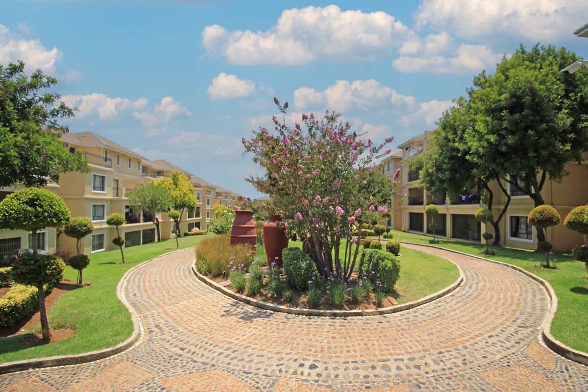 A well-maintained communal garden area featuring a circular paved driveway surrounded by landscaped greenery and multi-story apartment buildings.