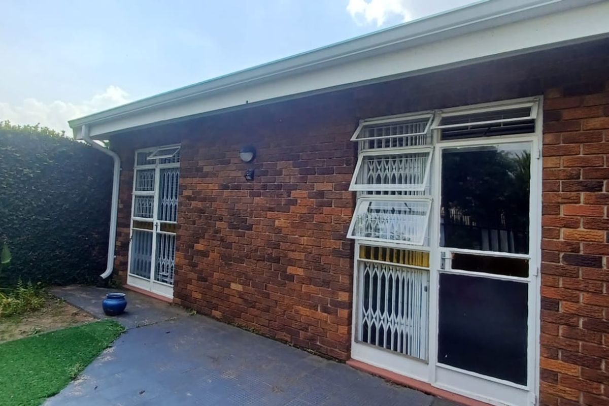 A rear exterior view of the townhouse featuring a brick facade, security gates on doors, and a paved patio area adjacent to a small garden.