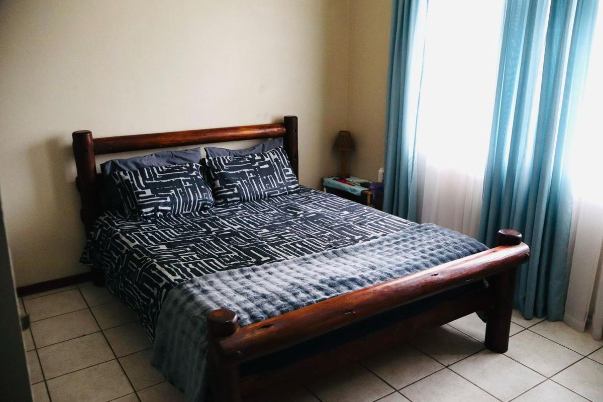 A standard bedroom featuring tiled flooring and natural light through a window with curtains.