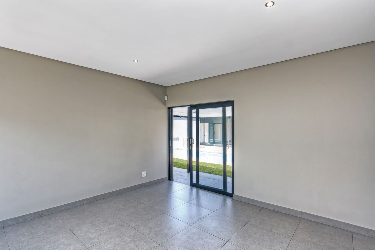 A bright, empty living space featuring neutral walls, modern grey floor tiles, and sliding glass doors providing direct access to the outdoor area.