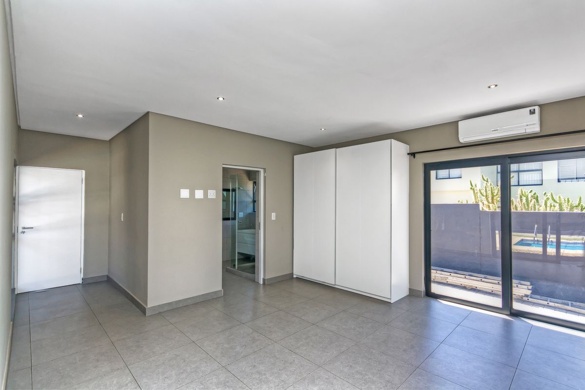 A bright bedroom featuring tiled flooring, built-in cupboards, an en-suite bathroom, and sliding glass doors leading to an outdoor area with a pool.