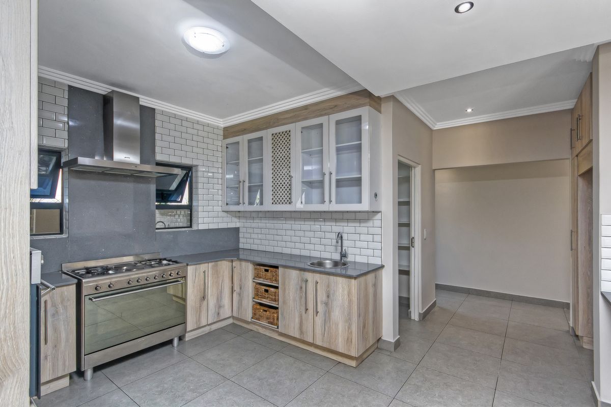 Modern kitchen featuring light wood cabinetry, subway tile backsplash, stainless steel gas stove with extractor fan, and an adjacent walk-in pantry.