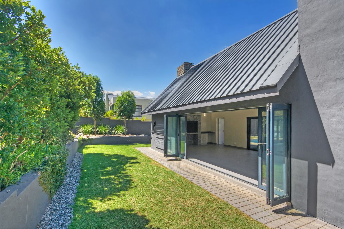 A view of the rear garden featuring a paved patio area with seamless indoor-outdoor flow through large folding glass doors.