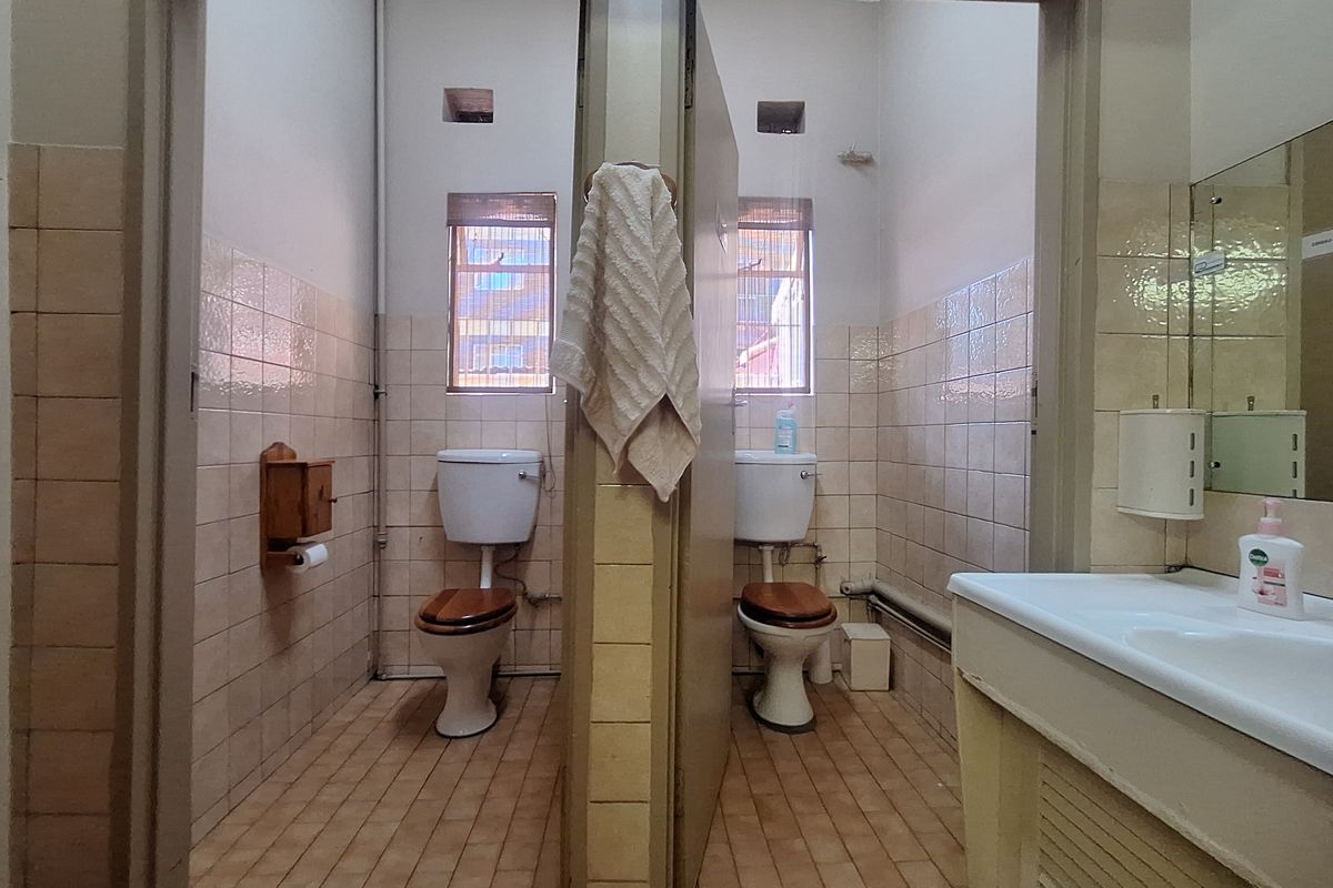 A shared bathroom facility featuring dual toilets, tiled wall and floor finishes, and a vanity basin with a wall-mounted mirror.