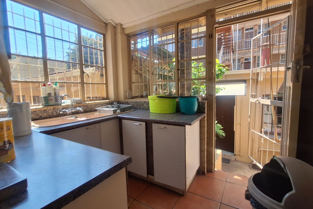 A compact kitchen area featuring laminate countertops, a stainless steel sink, and tiled flooring, with direct access to an outdoor area through a security gate.