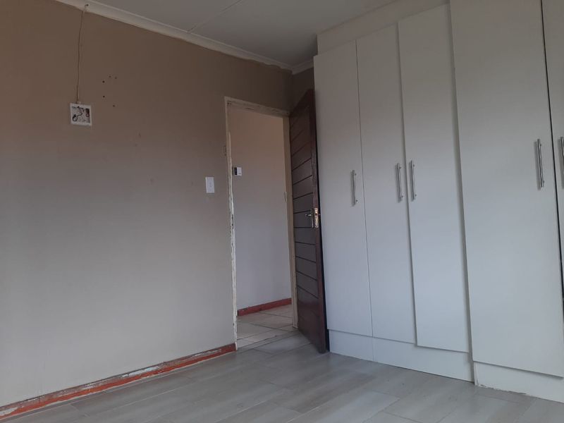 An empty bedroom featuring built-in white cupboards and light-toned laminate flooring, requiring minor cosmetic repairs to walls and skirting.