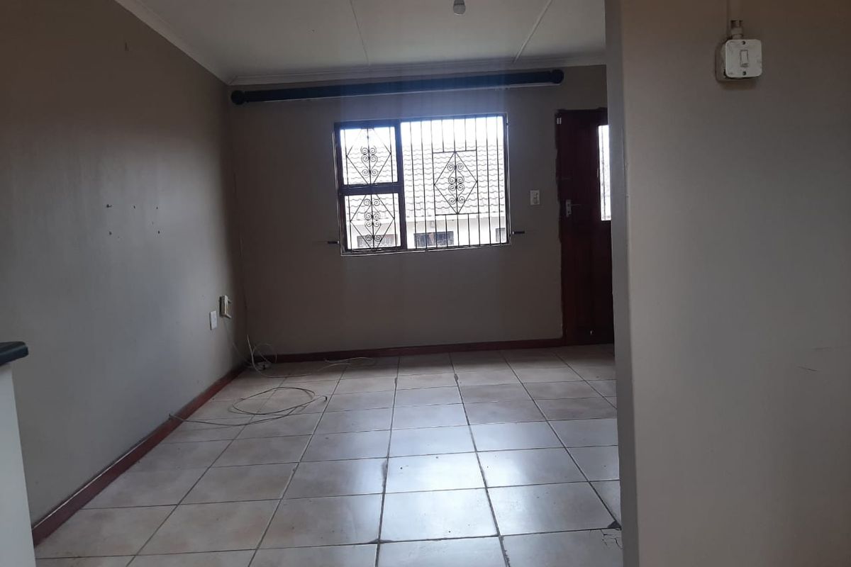 An empty living room featuring tiled flooring, security bars on the window, and neutral wall finishes, ready for personalization.