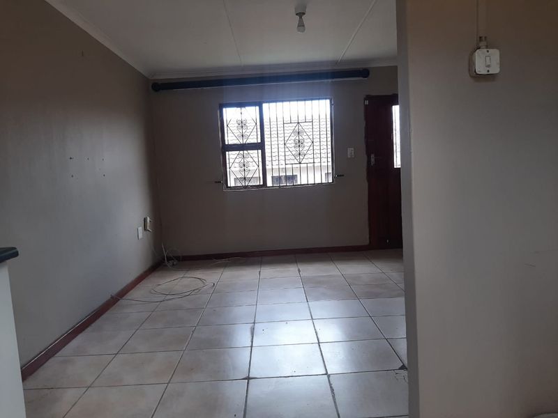 An empty living room featuring tiled flooring, security bars on the window, and neutral wall finishes, ready for personalization.
