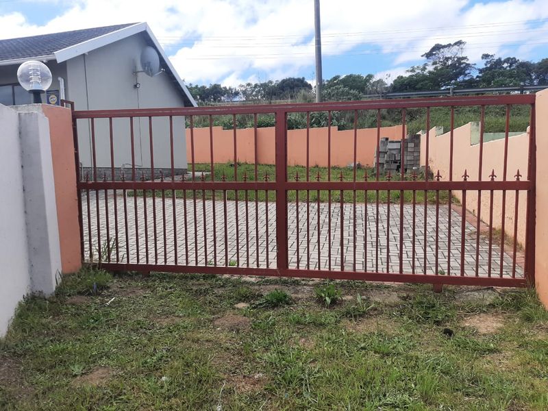 A view of the property entrance featuring a metal driveway gate, paved driveway, and perimeter boundary wall.