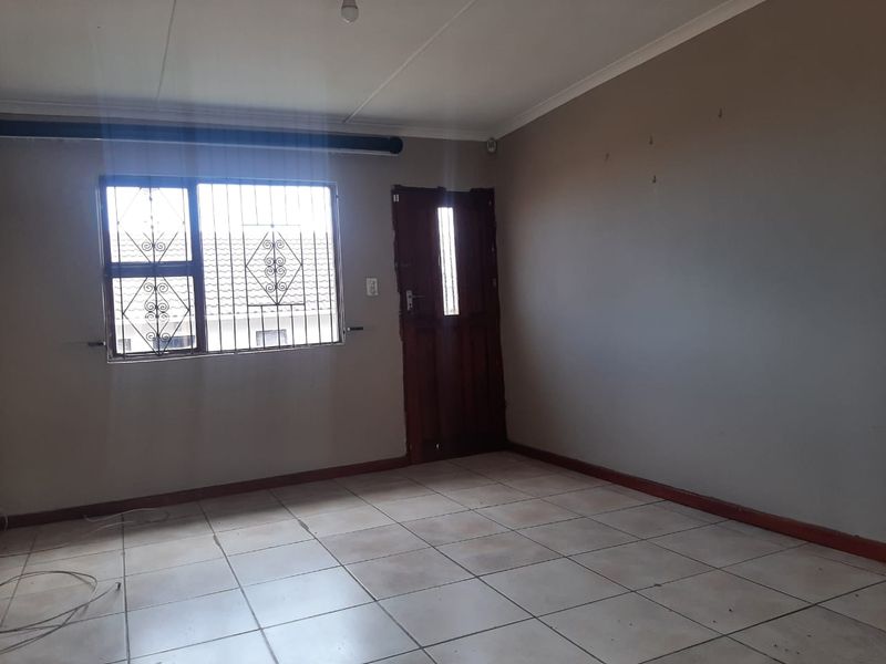An empty living room featuring tiled flooring, a timber entrance door, and security bars on the window, ready for a fresh update.