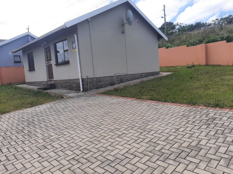 Exterior view of a residential house featuring a paved driveway, brick plinth detailing, and a secure perimeter wall.