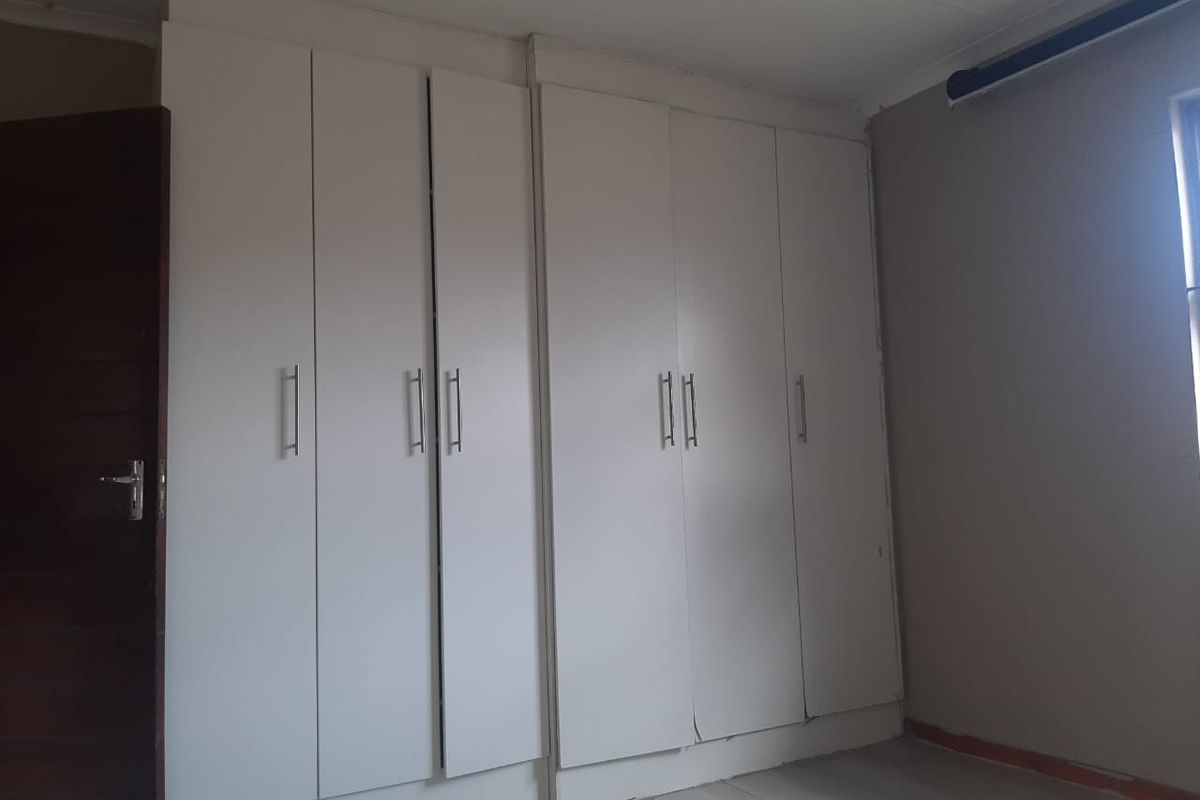 A bedroom featuring built-in white cupboards and tiled flooring, currently vacant and awaiting cosmetic updates to the finishes.