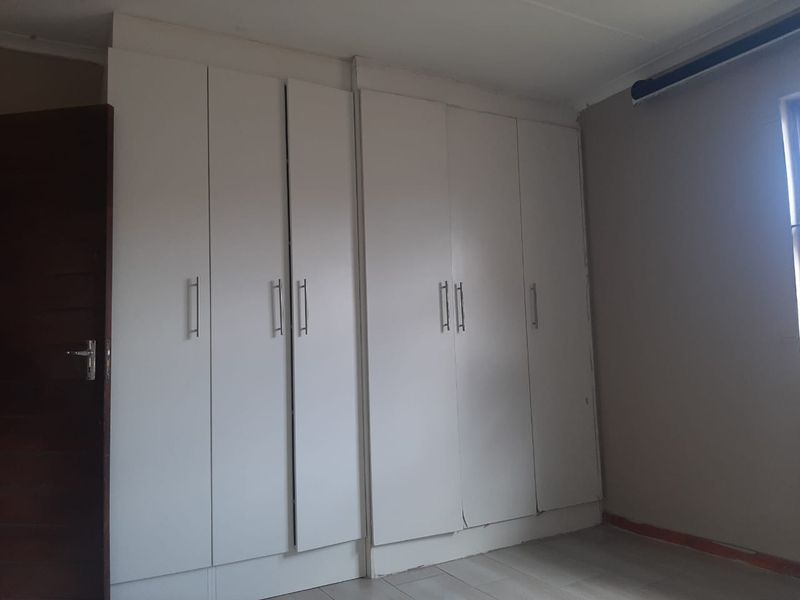 A bedroom featuring built-in white cupboards and tiled flooring, currently vacant and awaiting cosmetic updates to the finishes.