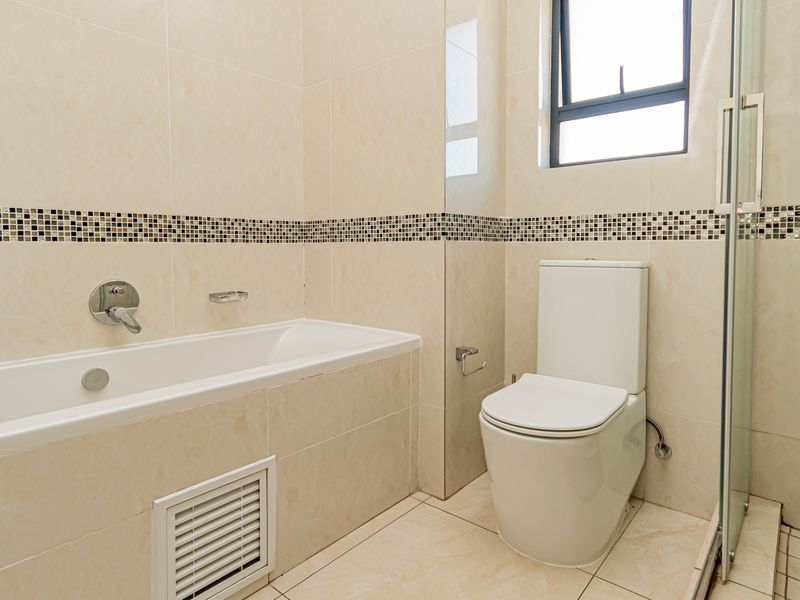 A clean, modern bathroom featuring a built-in bathtub, a separate glass-enclosed shower, and neutral floor-to-ceiling tiling with a decorative mosaic accent border.