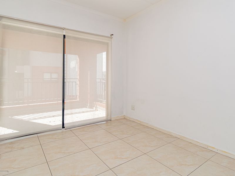 An empty bedroom featuring neutral ceramic floor tiles and a large sliding glass door providing access to an outdoor balcony area.