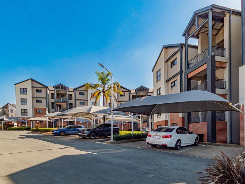 Exterior view of an apartment complex featuring multi-story brick buildings, paved parking areas, and covered shade cloth carports for residents.