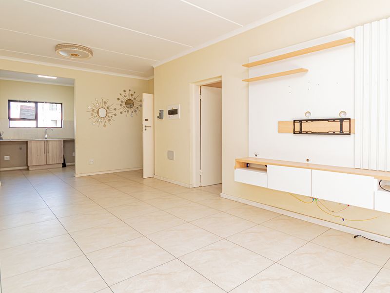 Spacious open-plan living area featuring neutral tiled flooring, a built-in media unit, and a view through to the functional kitchen space.