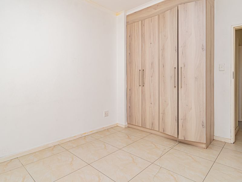 A bright, empty bedroom featuring neutral tiled flooring and a modern built-in wardrobe with light wood-grain finish.