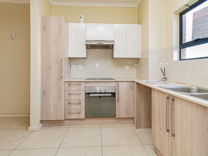 A clean, modern kitchen featuring light wood-grain cabinetry, built-in oven and hob, extractor fan, and double sink with tiled flooring and splashbacks.