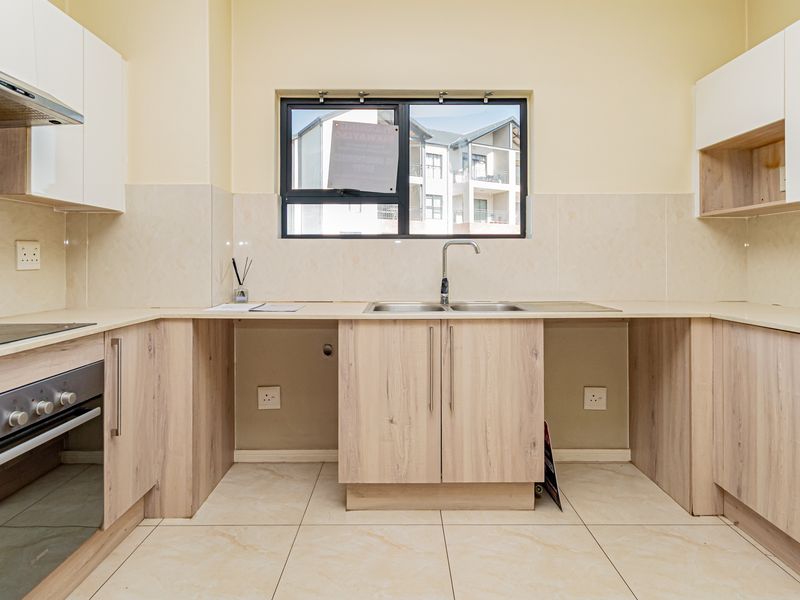 A modern, empty kitchen featuring light wood-finish cabinetry, integrated appliances, tiled splashbacks, and neutral floor tiles, offering a clean and functional workspace.