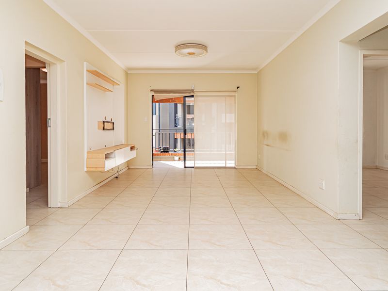 An empty, open-plan living area featuring neutral tiled flooring, a built-in media console, and direct access to a balcony through sliding glass doors.