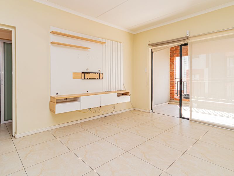 A bright, empty living room featuring tiled flooring, a built-in media console, and a sliding glass door leading to an outdoor balcony area.