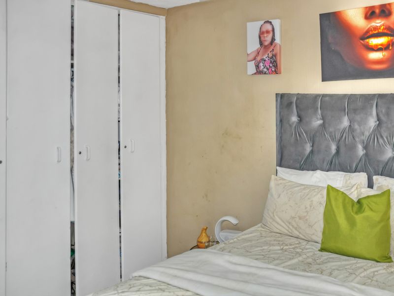 A bedroom featuring a built-in wardrobe and a grey tufted headboard, showing signs of wear on the wall surfaces.