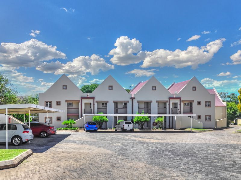 Front elevation of a multi-unit apartment complex featuring pitched roofs, private balconies, and covered carport parking spaces on a paved driveway.