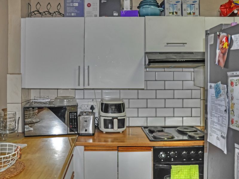 A compact kitchen featuring white cabinetry, subway tile backsplash, wooden countertops, and integrated cooking appliances.