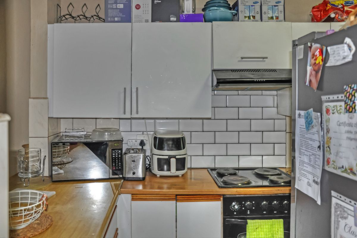 A compact kitchen featuring white cabinetry, subway tile backsplash, wooden countertops, and integrated cooking appliances.