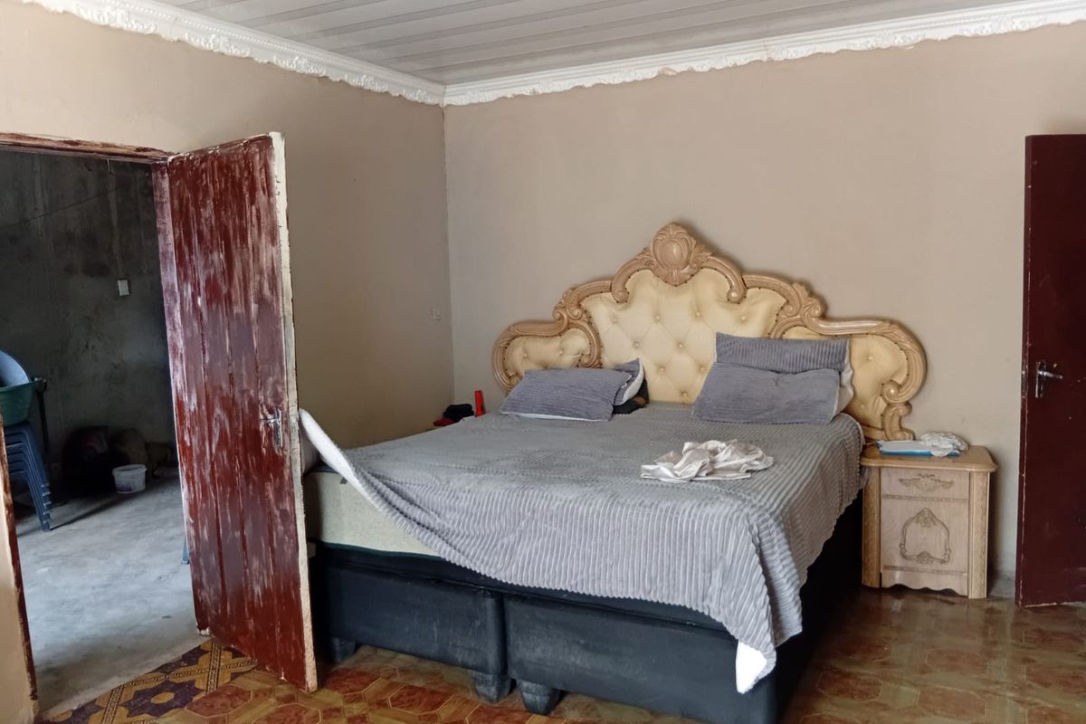A bedroom featuring decorative ceiling cornices and tiled flooring, showing signs of wear on the interior door and wall finishes.