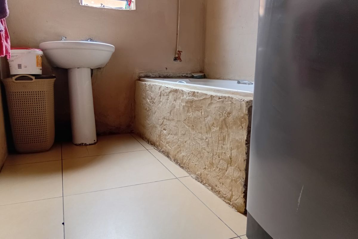 A bathroom featuring a pedestal basin and a built-in bathtub with an unfinished surround, requiring cosmetic updates and repairs to wall finishes.