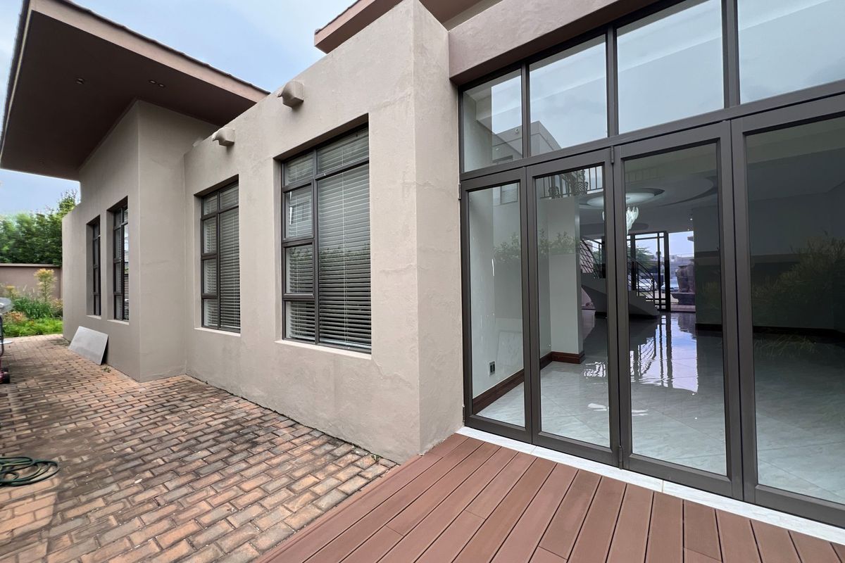Rear exterior view featuring a modern facade, large glass sliding doors, and a composite timber deck leading to a paved patio area.