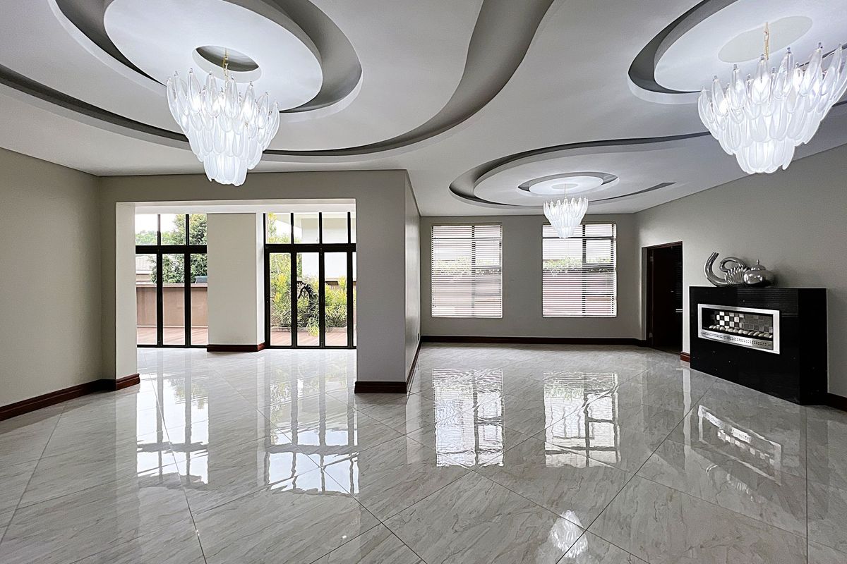 Spacious living area featuring high-gloss tiled flooring, intricate recessed ceiling design with modern chandeliers, and a built-in fireplace, opening onto an outdoor patio.
