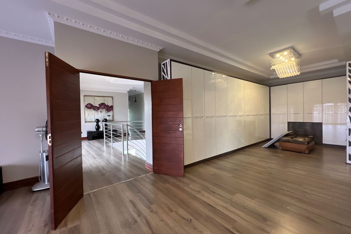 Spacious bedroom featuring extensive built-in high-gloss cabinetry, recessed ceiling detailing, and modern timber-look flooring, with double door access to the hallway.