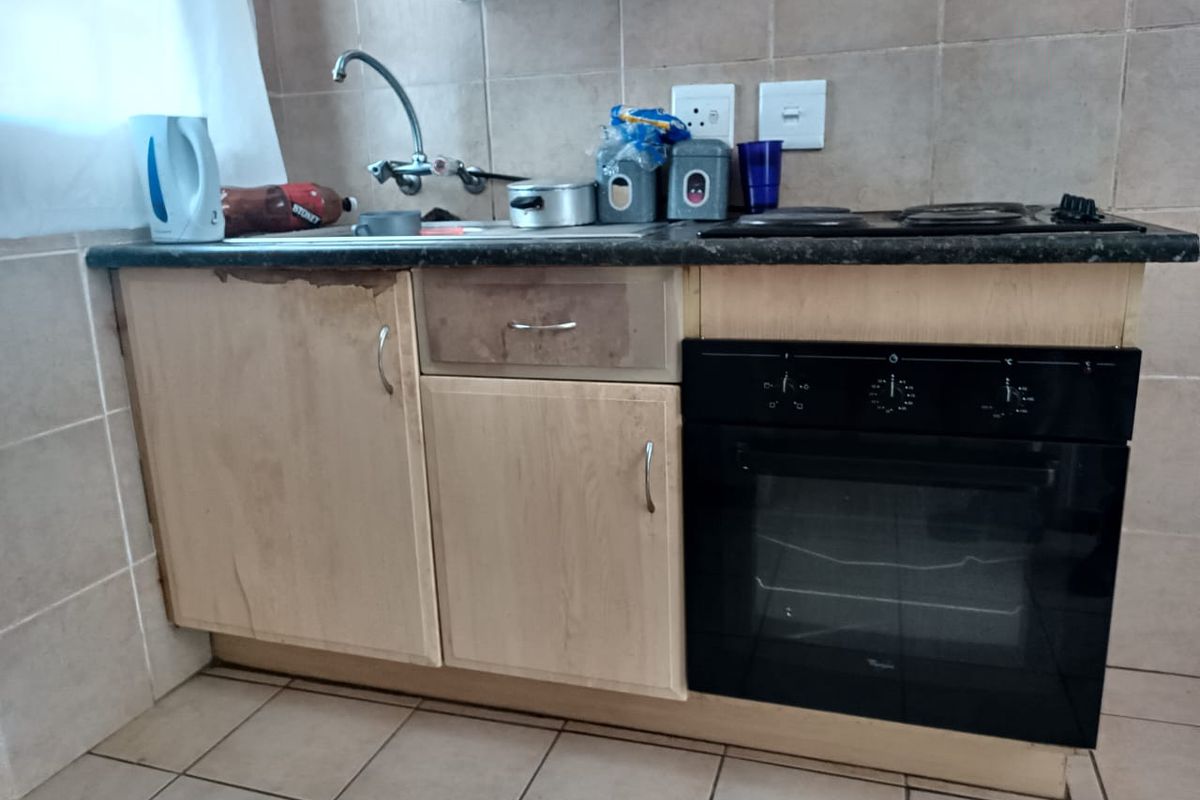 Compact kitchen area featuring built-in cabinetry, a stainless steel sink, and a fitted electric oven with a hob.
