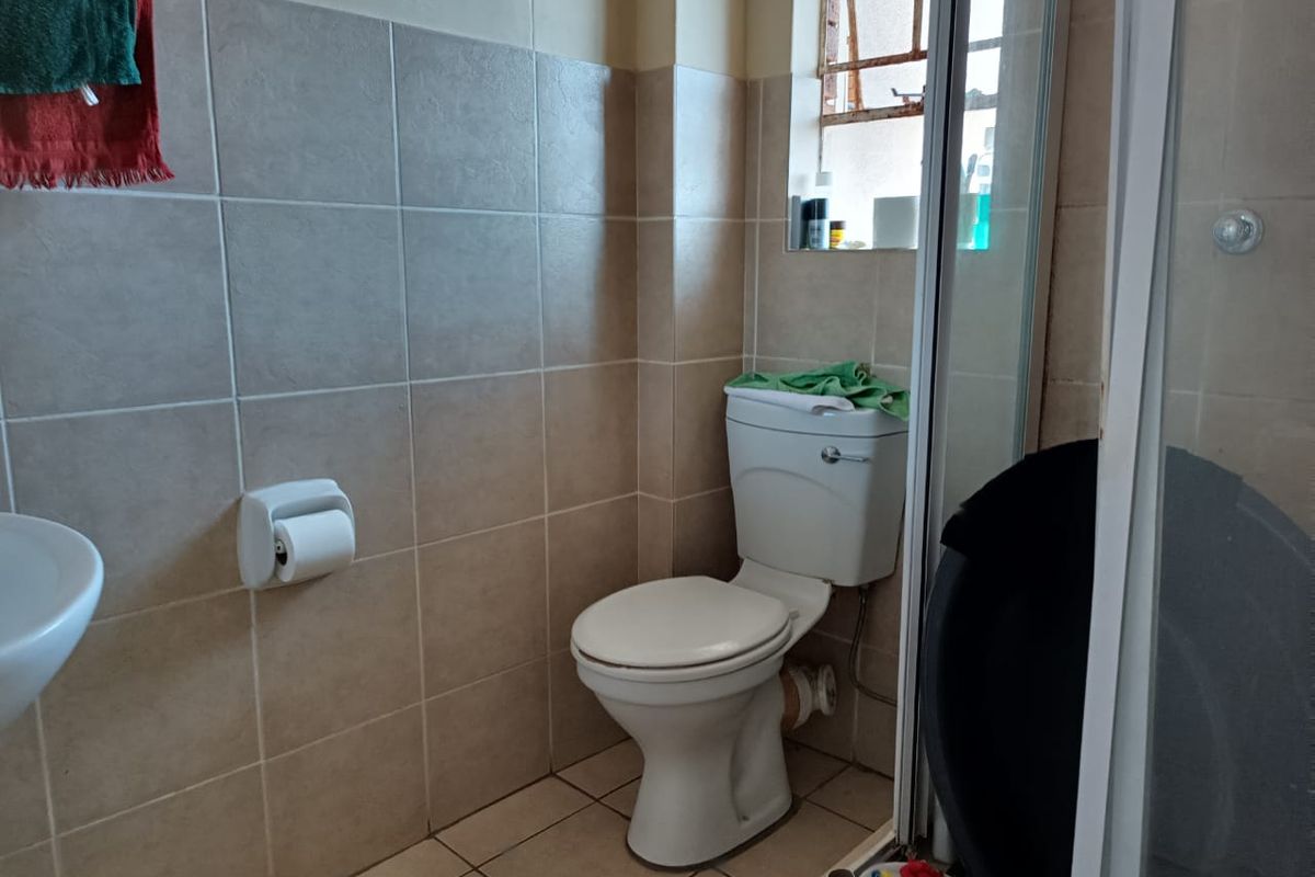 A functional bathroom featuring a standard toilet, wall-mounted basin, and a shower enclosure with tiled walls and flooring.