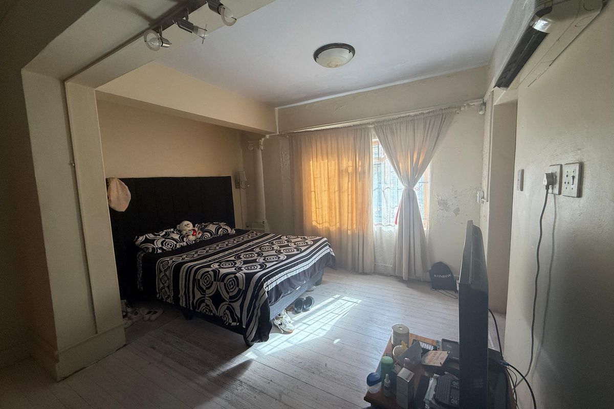 A bedroom featuring timber flooring, track lighting, and a wall-mounted air conditioning unit, showing signs of wear on the wall surfaces.