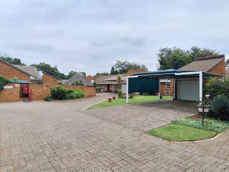 A view of the townhouse complex entrance featuring paved driveways, covered parking carports, and brick-built garage structures.