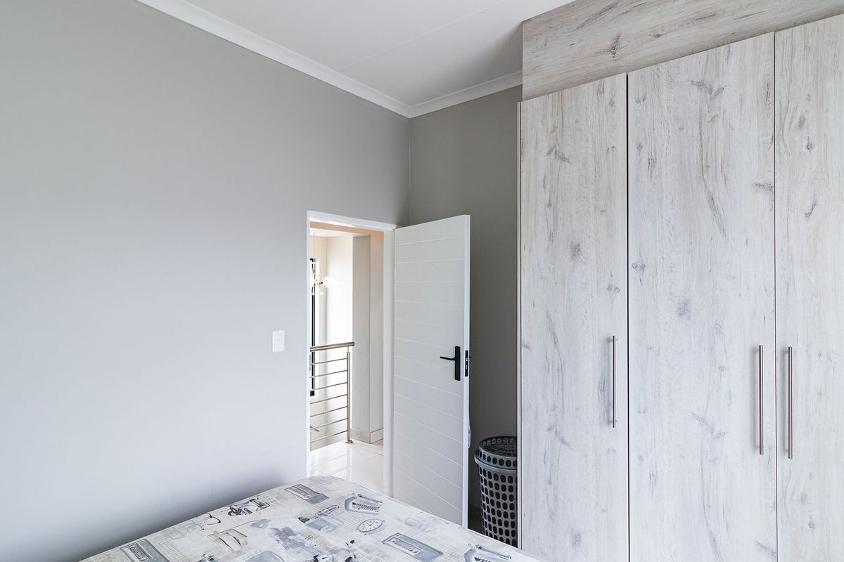 A well-maintained bedroom featuring neutral grey walls and modern wood-grain built-in cupboards with sleek metal handles.
