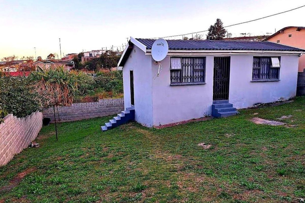 Rear view of a detached house featuring a corrugated metal roof, security bars on windows, and a surrounding perimeter wall with a grass yard.