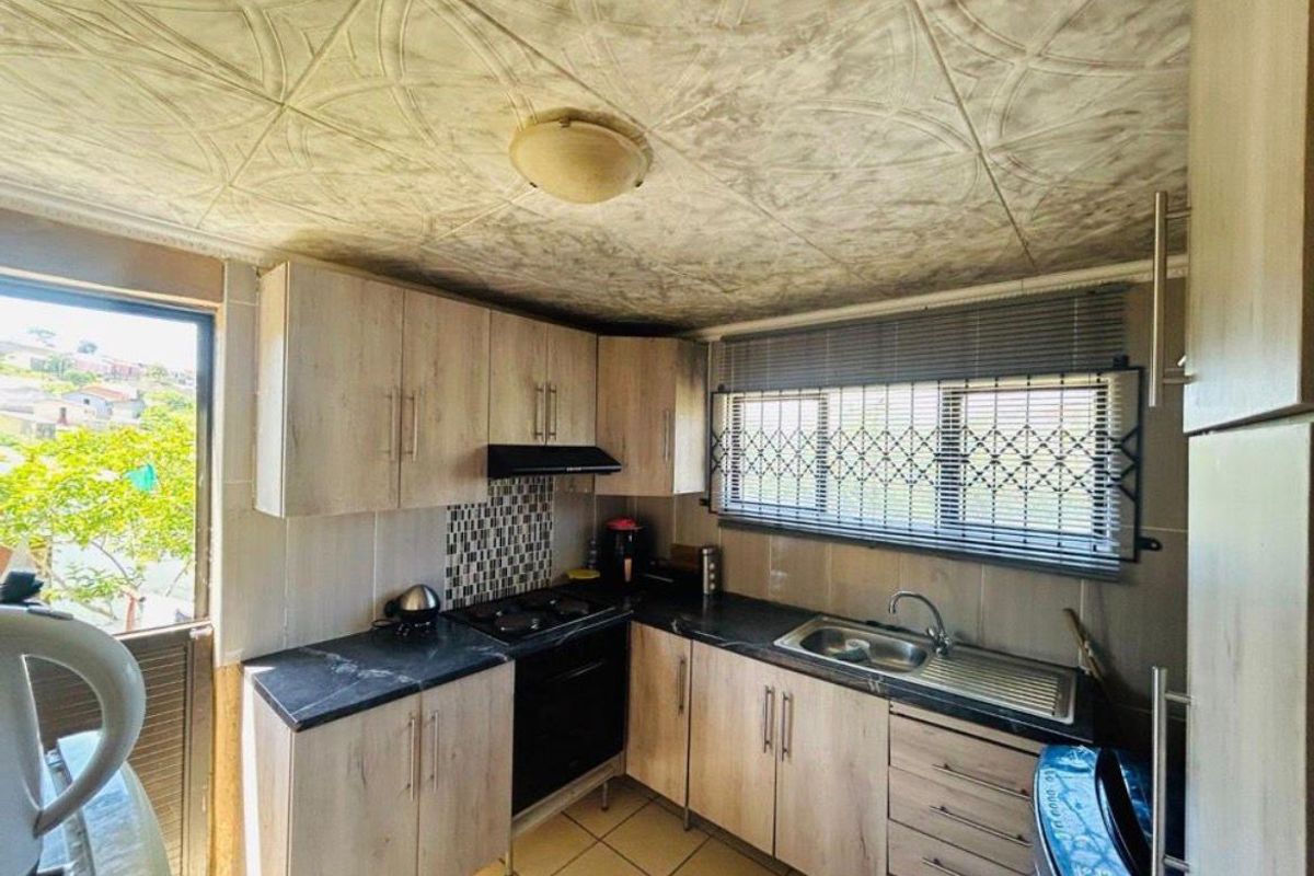 Compact kitchen featuring light wood-finish cabinetry, dark laminate countertops, built-in oven with extractor, and tiled flooring with direct access to the exterior.