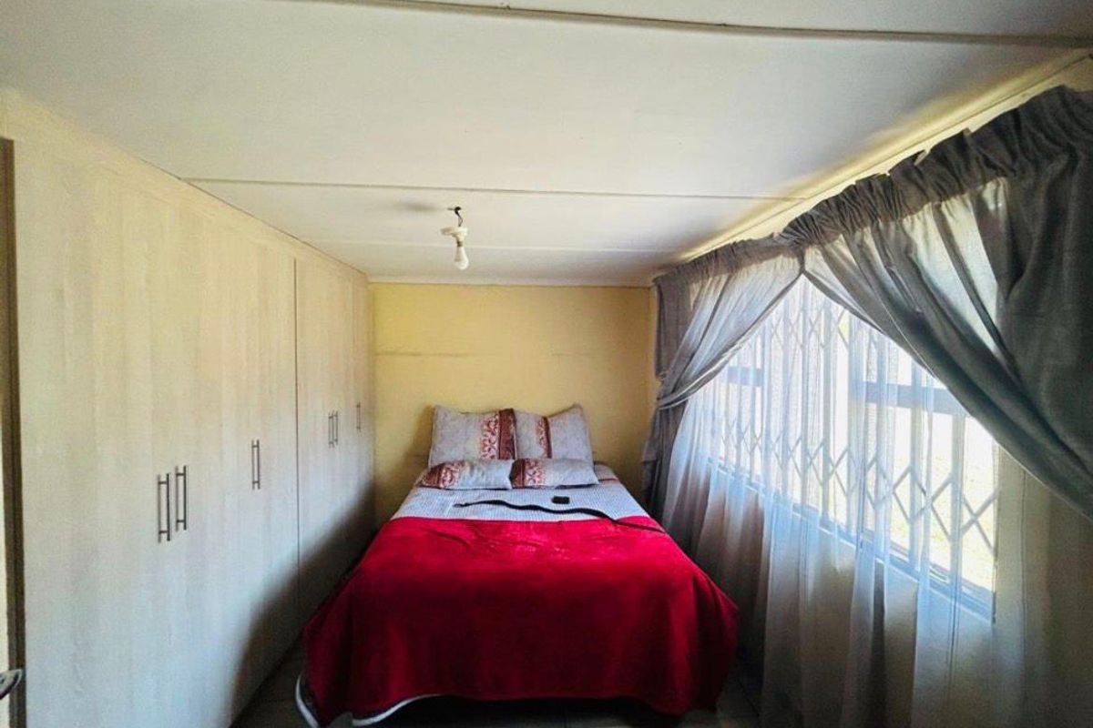 A compact bedroom featuring built-in cupboards, tiled flooring, and a window fitted with a security gate.