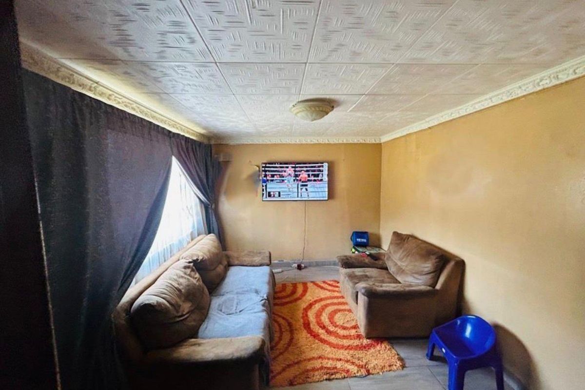 A living room featuring textured ceiling tiles, decorative cornice, and tiled flooring, currently requiring cosmetic updates to the wall finishes.