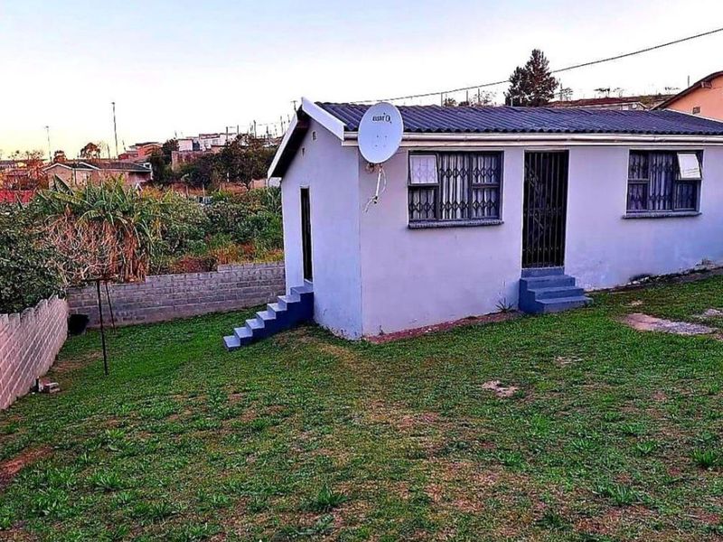 Rear view of a detached house featuring a corrugated metal roof, security bars on windows, and a surrounding perimeter wall with a grass yard.