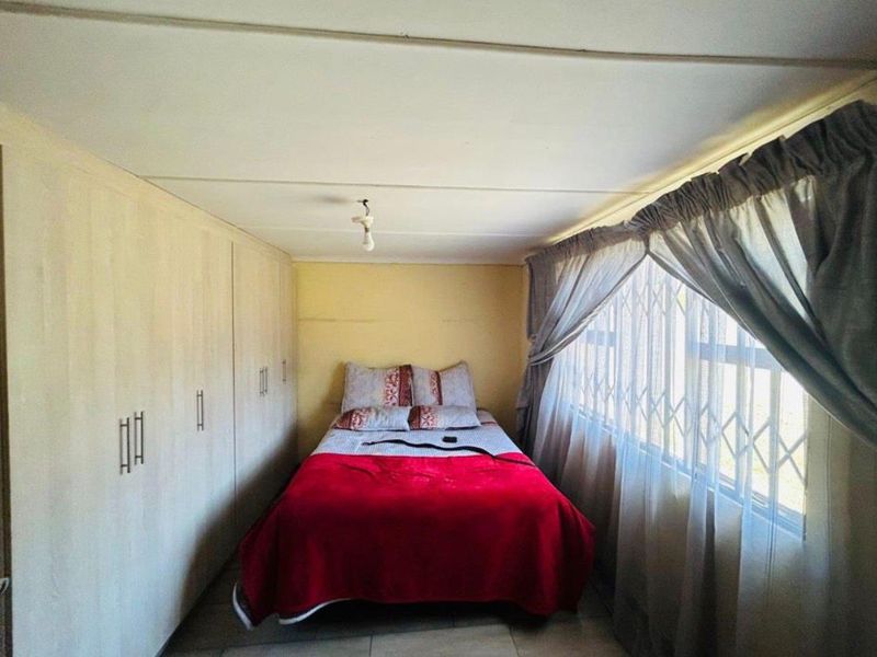 A compact bedroom featuring built-in cupboards, tiled flooring, and a window fitted with a security gate.